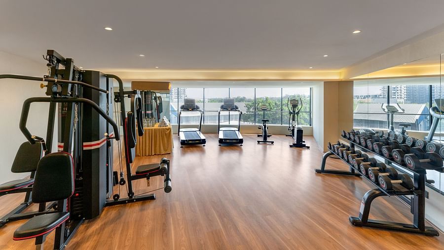 Modern gym with wood floor, diverse equipment including treadmills and weights, large windows offering city views at Clarks Inn Suites, Hyderabad
