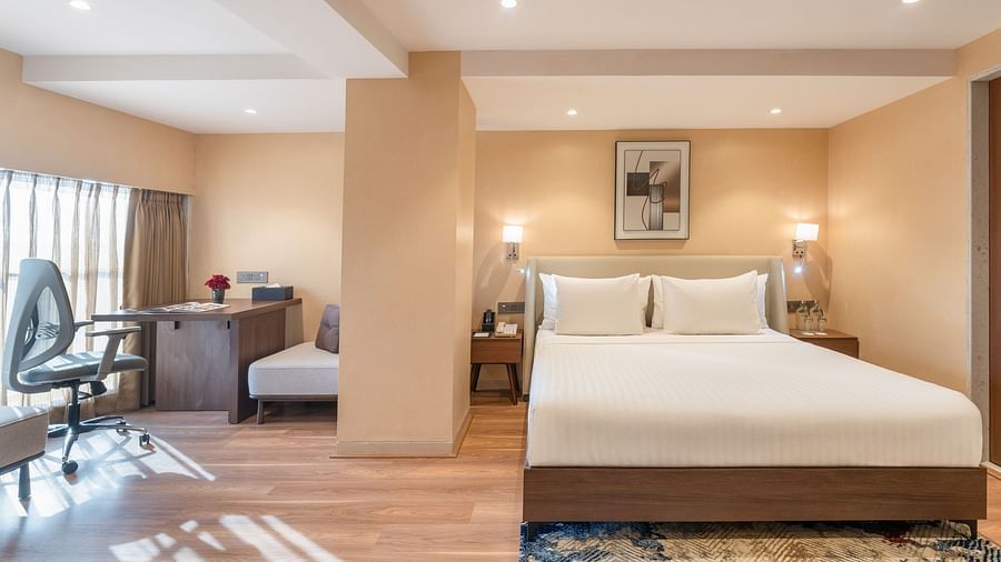 Elegant hotel room with plush king-size bed, soft lighting, wood flooring, and a study area with an office chair at Clarks Inn Suites, Hyderabad