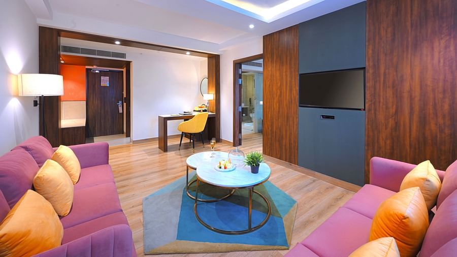 An image of a seating area with sofa sets, tea table at the centre,  work desk  with chair, and a flat TV screen - Golden Tulip, Agra