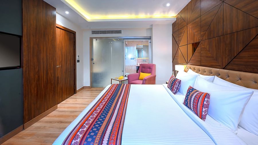 An image of a bedroom with double size bed, bedside table next to it which has a lamp and a telephone on it, and at one corner there is a sofa and tea table - Golden Tulip, Agra