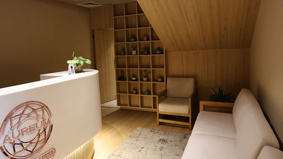 Spa reception area with wood decor, a white desk with 'Aureum Wellness' logo, cosy seating, potted plants, and a shelf with small decorative items - Golden Tulip, Lucknow