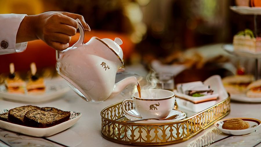 A sophisticated high tea arrangement with a white teapot pouring tea into a fine china cup, accompanied by pastries, sandwiches, and elegant tableware
