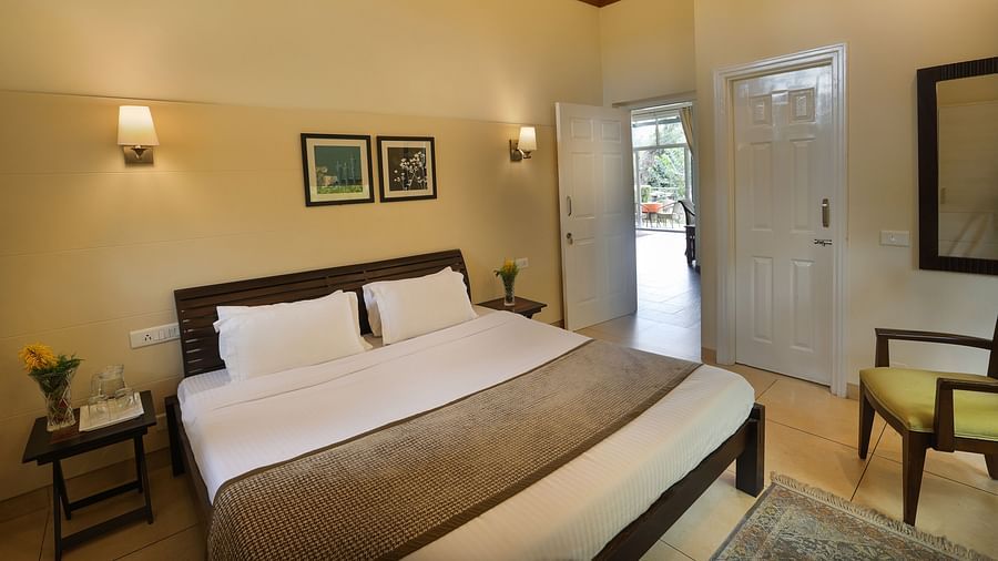 a king size premium bed with white lines with pillows and an entrance door on the right - Lamrin Norwood Green, Palampur