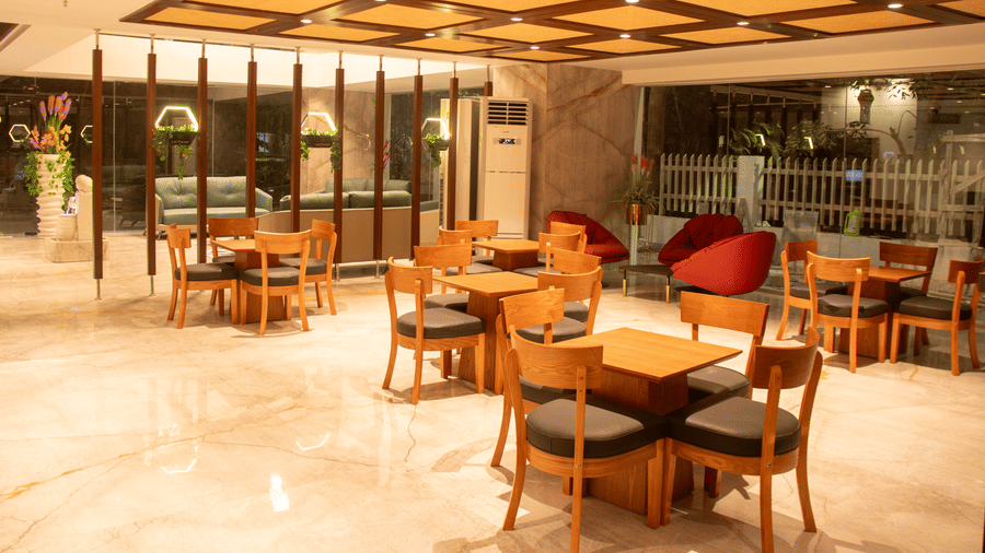 A hotel lobby area space with arranged tables and chairs, large windows, and patterned ceiling panels with lighting.