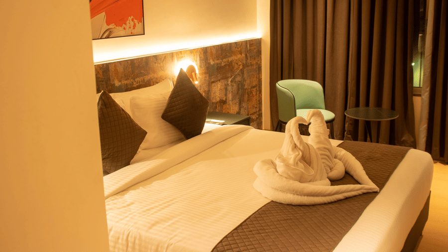 A bedroom with king size bed, bedside lamps, chair, table, wall art, and folded towel decor at Magnus Lxia Premier, Kalyani Nagar.