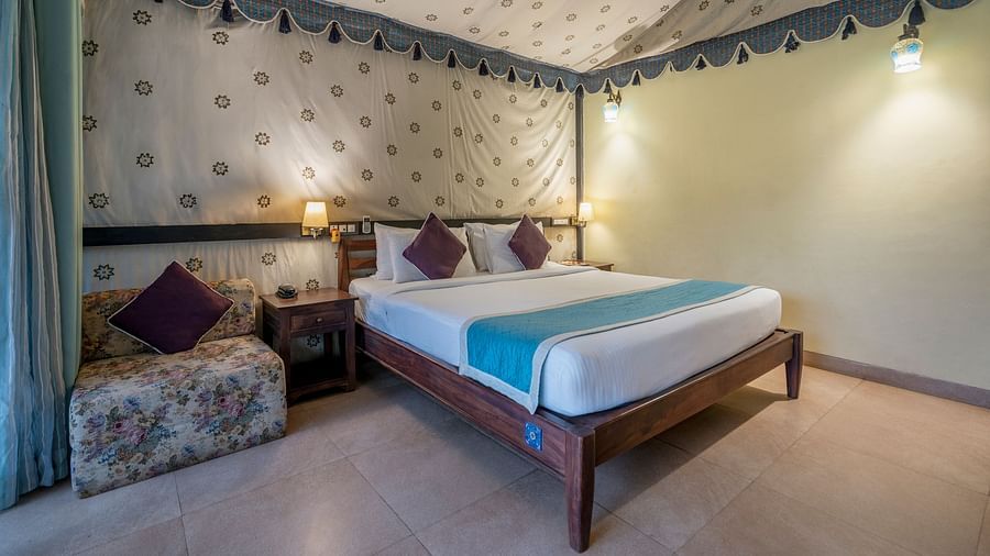 An image of a bedroom inside a tent  which has king size bed and a wooden sofa