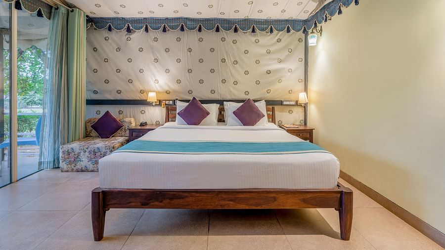 An image of a bedroom inside a tent  which has king size bed and a wooden sofa
