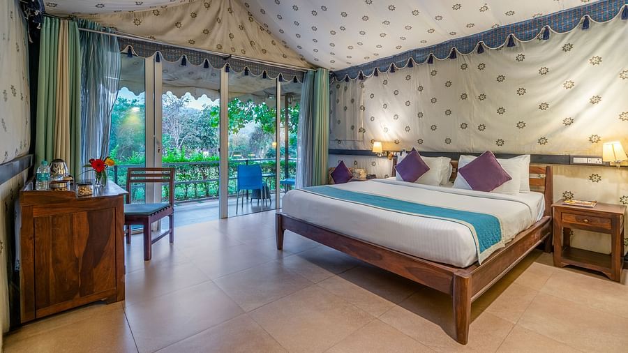 An image of a bedroom inside a tent  which has king size bed and a wooden sofa