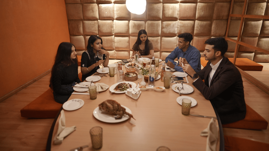 A group of people dining at a restaurant table at Park Plaza Ludhiana with padded wall panels overhead warm lighting and food and drinks placed on the table.
