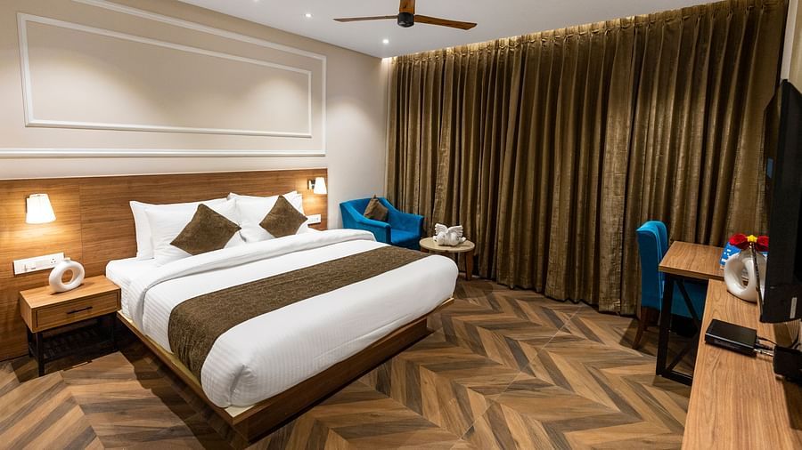 Superior Room at Pride Hotel Rishikesh featuring a plush bed facing the TV mounted on the wall and a sitting space next the window covered by curtains