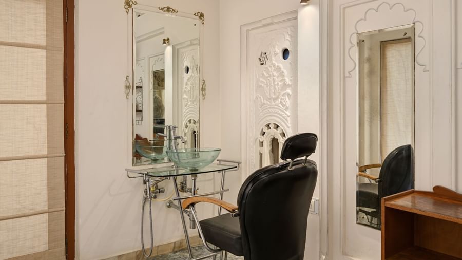 Elegant salon corner at Ram Pratap Palace, Udaipur with vintage mirror, glass basin, ornate wall design, and classic black barber chair.