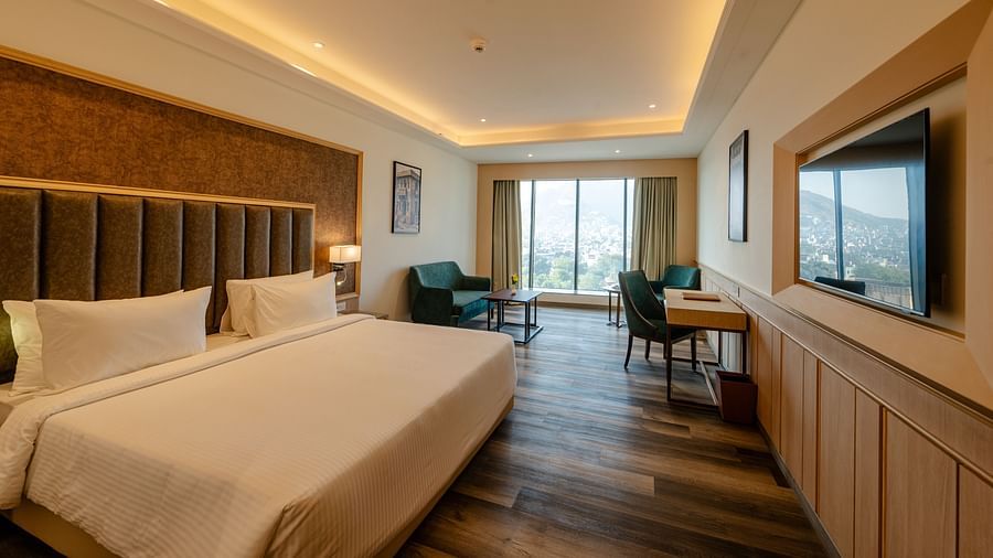 An image of our premium room in Ajmer featuring warm lighting, a king size bed, cosy furniture, a television and views of the city - Sarovar Portico, Ajmer