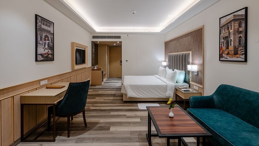 A hotel room featuring a king size bed, a seating area with teal coloured sofas and a writing desk - Sarovar Portico, Ajmer