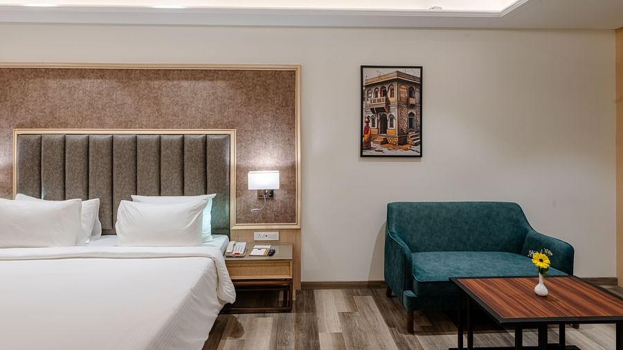 A room with a king size bed, a teapoy, a teal coloured sofa and ambient lighting - Sarovar Portico, Ajmer