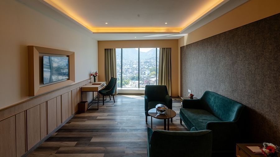 A living area in a hotel room in Ajmer featuring a teal coloured sofa set, a wall-mounted television, and panoramic views of the city - Sarovar Portico, Ajmer  