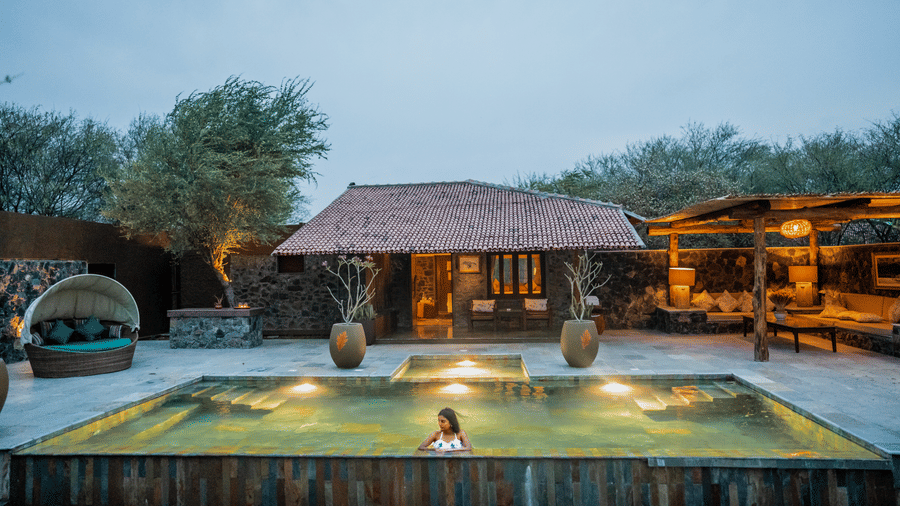 Swimming pool of The Blackbuck Lodge, Velavadar featuring a cottage and evening lighting.