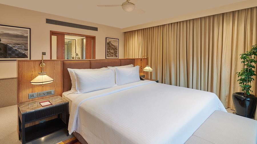 A comfortable bed with a side table, a potted plant, curtains and wall decor at The Dukes Retreat.