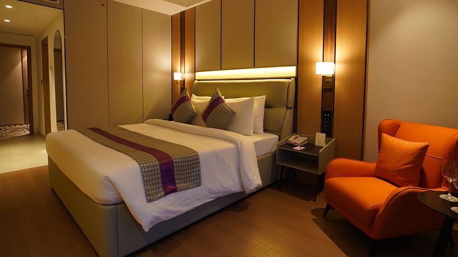 A cosy hotel club room features a single bed with patterned linens, an orange armchair with a side table, and warm lighting from bedside lamp - The Orchid Hotel, Chandigarh