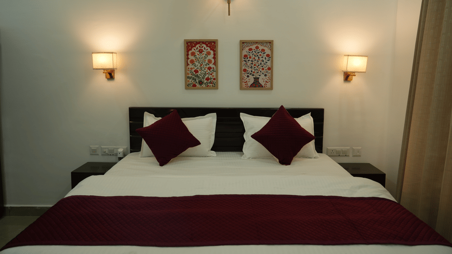 Comfortable guest room featuring a king size bed, maroon accents, framed artwork and warm lighting.