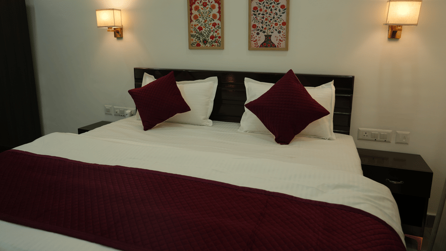  Guest room with a king size bed, maroon cushions, decorative artwork and warm bedside lighting.