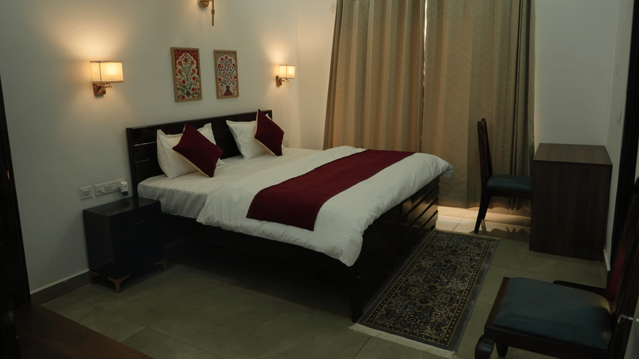 Room with a king size bed, maroon accents, bedside tables, curtains and warm lighting.