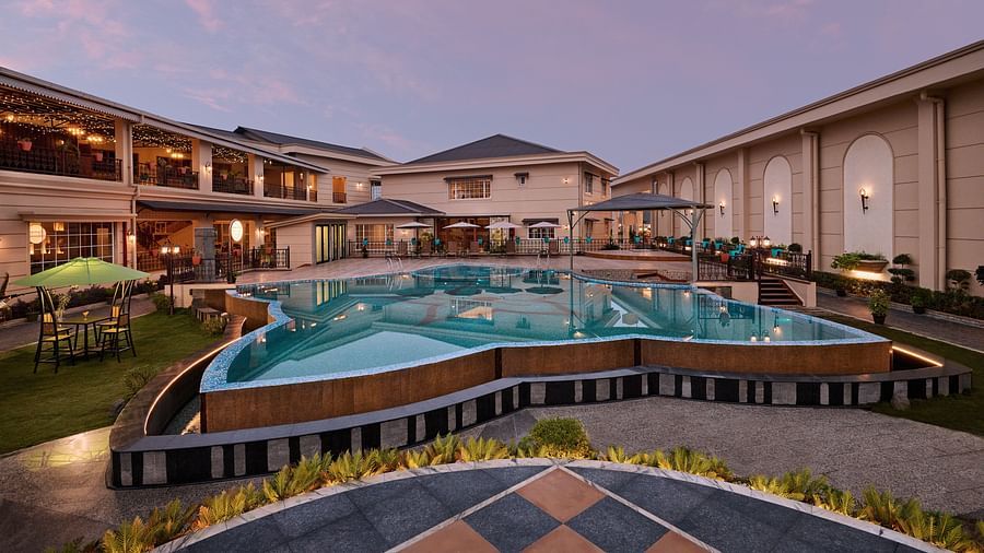 A large, uniquely shaped swimming pool reflects the soft colours of the twilight sky at a resort. Buildings with illuminated balconies and outdoor seating surround the pool area, which is bordered by landscaping and paved walkways - Voyage The Solitaire Bl