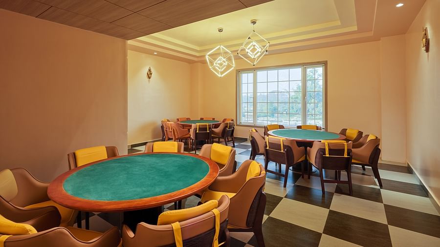 Indoor recreational room with multiple round card tables, cushioned chairs, modern lighting fixtures, and large windows letting in natural light - Voyage The Solitaire Bliss.