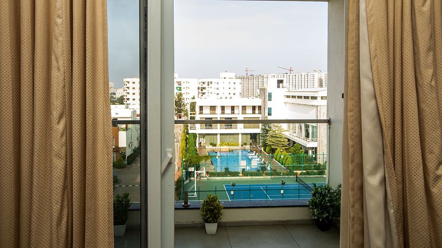 View from the room into a balcony with small plant pots and an open-air swimming pool