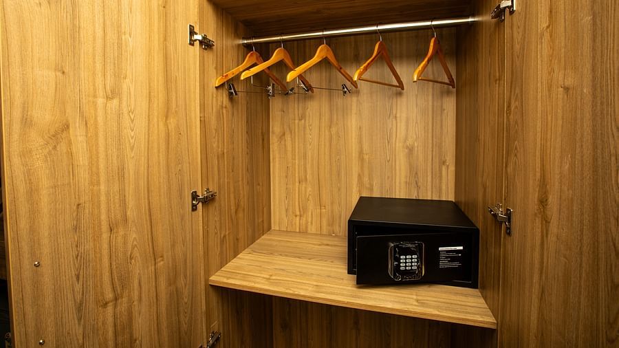 Wooden-finished wardrobe in the hotel room with hangers and a secure locked box