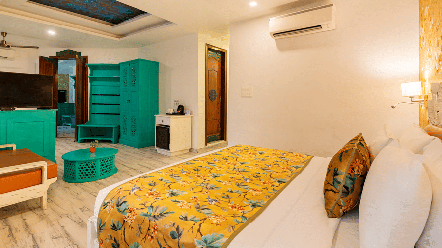 A spacious suite featuring a bed, an attached bathroom, a television facing the bed, an A/C unit, a ceiling fan, and furniture next to an open door | Summit by the Ganges Beach Resort & Spa, Rishikesh