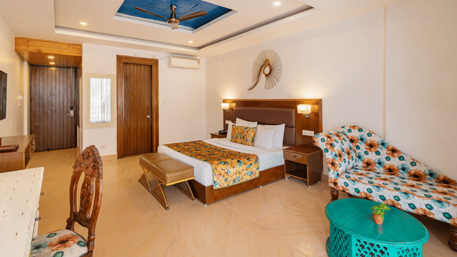 A bedroom featuring a neatly made bed, a bedside table, a sofa, a coffee table, a desk with a chair, and an art piece on the wall | Summit by the Ganges Beach Resort & Spa, Rishikesh