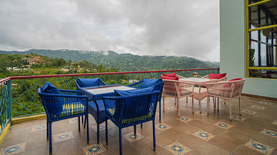 A balcony seating area with tables and chairs facing hills and cloudy sky on a terrace at Adrushya Estates, Mukteshwar.