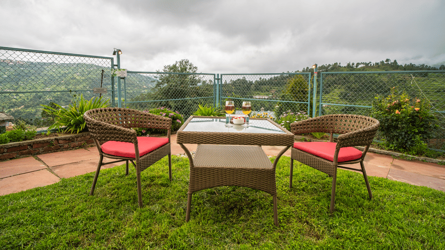An outdoor seating setup with chairs and a table placed on grass facing a valley view at Adrushya Estates, Mukteshwar.