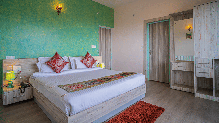 A bedroom with a king size bed, wall lights, wardrobe, and side tables items arranged indoors ready to be booked with exclusive offers at Adrushya Estates, Mukteshwar