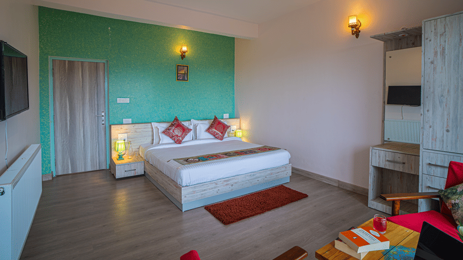 A bedroom with a king size bed, wall lights, vanity, side tables,, and television, arranged inside at Adrushya Estates, Mukteshwar.