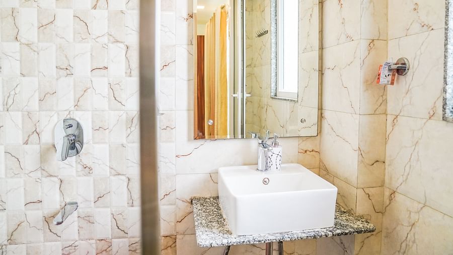 A modern bathroom with a white sink, a mirror, and a shower area, featuring neutral tones - Asian Suites Cyber Park, Gurgaon