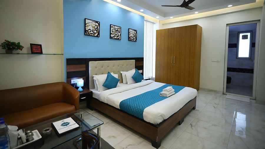 A room with a double bed, a sofa, a coffee table, a ceiling fan, and framed artwork on the wall - Asian Suites Cyber Park, Gurgaon