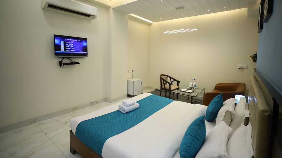 A room with a double bed, a television mounted on the wall, a chair, and modern lighting fixtures - Asian Suites Cyber Park, Gurgaon