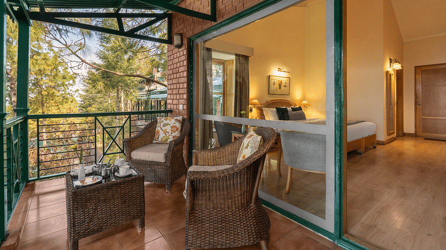 A balcony featuring two wooden chairs and a small table, offering a view of the room interior and the surrounding scenery
