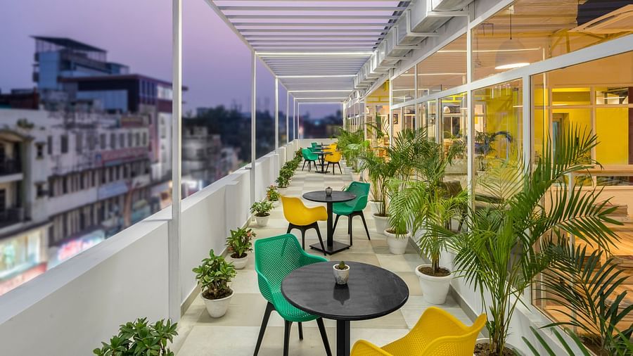 An image of a rooftop outdoor seating area featuring multiple chairs and tables, captured in the evening with lights illuminated.