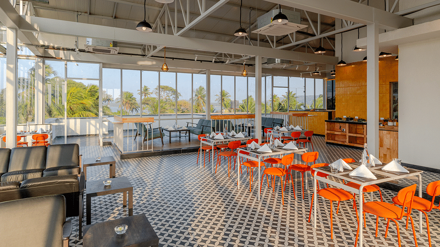  spacious and airy restaurant with industrial-style exposed ceiling, large windows letting in natural light, and a color palette of orange and grey, providing a relaxed dining atmosphere  at Bedzzz Xclusiv Morjim, Goa