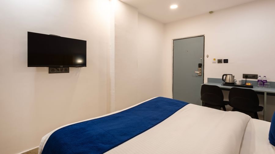 A Deluxe Room with a bed, a wall-mounted television, and a desk area with a chair and what appears to be a mini-fridge or coffee station. - Beestay Hotels Financial District, Hyderabad 