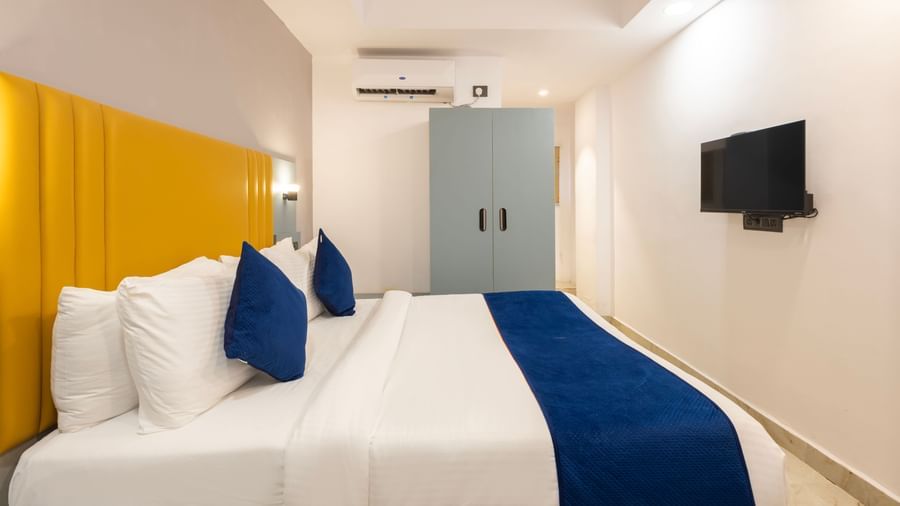 Side view of a Deluxe Room with a bed, blue and white bedding, a yellow headboard, and a desk area - Beestay Hotels Financial District, Hyderabad 