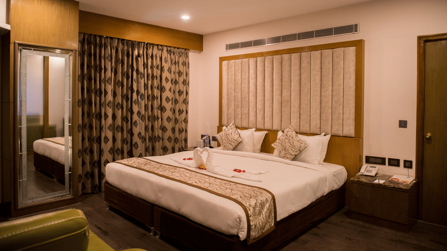 A hotel room at Benzz Park Chennai featuring a neatly made bed with white linens, a bedside table, and curtains.