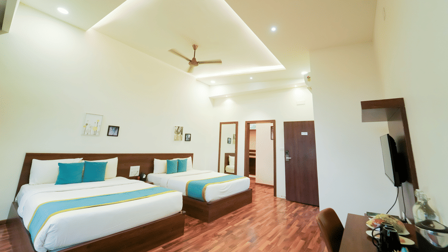 A bedroom at Bindiga Peak Resort showing two beds, bright ceiling lights, a ceiling fan, and wooden floors.