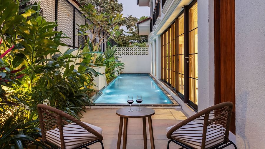 A tranquil poolside seating area with modern chairs, surrounded by lush greenery and warm villa lighting - BluSalzz Villas - Alocassia, Anjuna