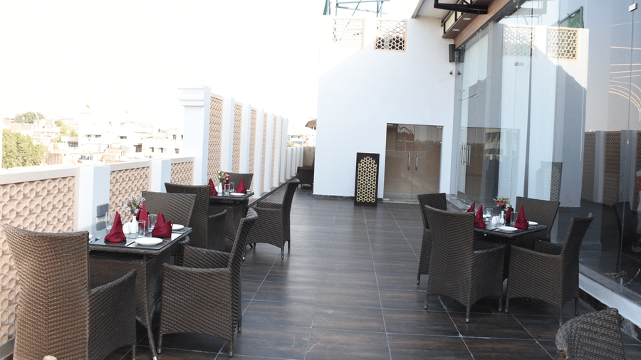 Outdoor seating area at Comfort Inn Sapphire by Eastlynn Collections, Jaipur with tables, chairs, railing, and open sky view.