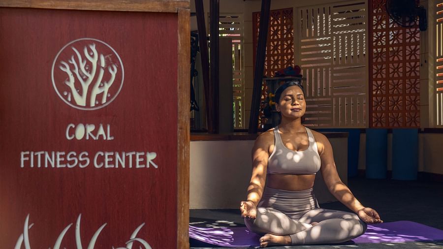 : A sign for the  Opal Fitness Center displayed alongside a statue of a person in a meditative pose. The background includes rustic wooden elements and a calm environment - Coral Reef Resort & Spa, Havelock