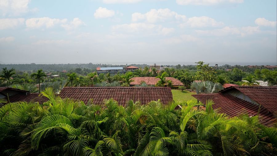 A panoramic view of lush greenery with traditional red rooftiles peeking out from the dense canopy, captured on a cloudy day - Crescent Resort, Goa