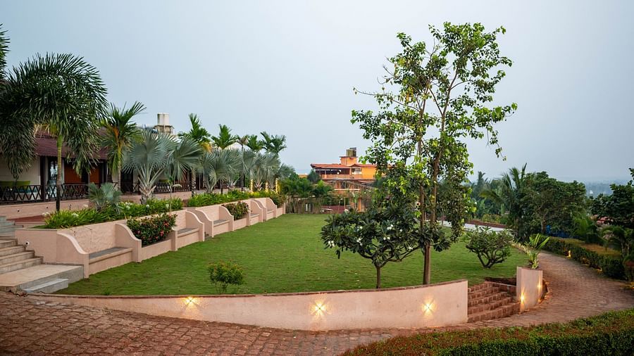 A landscape image showing a couple of trees in front of a building, situated on terraced grounds, with decorative lights adding charm to the scene - Crescent Resort, Goa